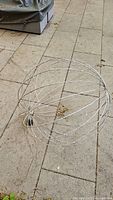 Light wireframe spherical garden orb showing its shape and resting on paved outdoor ground, visible minor wear and rust spots