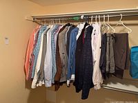 Multiple men's dress shirts and jackets hanging on a rack in a basement, varying in colors and patterns.