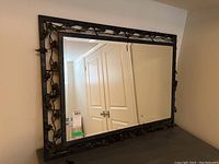 Front view of the rectangular mirror showing the metal leaf frame and bevel edges. Reflects double doors in the background.