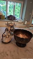 Silver plate serving bowl, condiment holder, salt and pepper shakers, and other items on marble table.