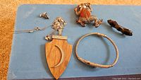 Lot overview showing multiple jewelry items including wooden pendant on chain, pins, bracelet, and stud earrings on blue surface.