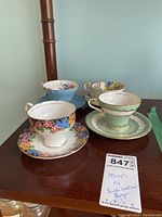 Photo showing four teacups with matching saucers arranged on wooden surface, floral and green pattern visible