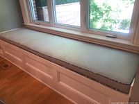 Long light beige window seat cushion with black and white trim, showing overall shape and condition including some small stains.