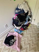 Stack of mixed women's clothing including sweatshirts and various tops, colors range from white, black, pink to blue.