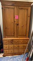 Front view of the Pulaski wooden armoire showing closed double doors with wood knob handles and bottom multiple drawers, set on blue tarp.