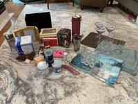 Photo showing assorted plastic glasses, cocktail shaker, candle jars, placemats, picture frames, coasters, and decorative items.