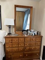Pulaski Furniture Corporation wooden dresser with attached mirror, displaying multiple drawers with round wooden knobs. The dresser is against a wall, decorated with a lamp and framed photos on top.