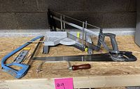 Photo showing four saws: manual miter saw, blue hacksaw, regular hand saw with black handle, coping saw with wooden handle and extra blades.