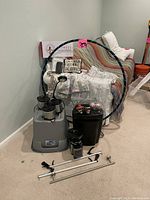 Photo of lot showing two hula hoops leaned against the wall, three small Crock pots stacked, black shredder, and halogen desk lamp on floor near couch with blankets and pillows.