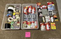 Photo showing two bins with many rolls of tape, several Command strip hanger packages and assorted shelf brackets and mounting hardware.