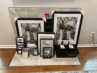 Photo showing a group of 39 picture frames arranged on floor against wall: large floral print frames, medium frames, small frames, and stack of black frames.