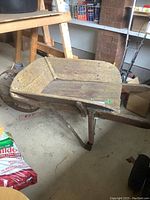 Side view of antique wooden wheelbarrow with iron wheel visible underneath, showing wooden tray with signs of wear and tear.