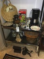 Full view of two lower metal shelves with various kitchen items including basket, coffee maker, grinder, cookie cutters, gloves, wooden bucket, metal track piece, boots, hat box.