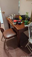 Image showing wooden desk from side with items on top and brown metal framed chair with cushioned seat in front of it.
