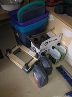 Photo of the pair of wood framed dollies, three storage totes in blue, purple, and dark gray stacked with lids, and several automotive fluid jugs in front and beside the totes.
