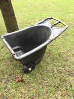 Side view of the black resin garden cart showing deep basin, handlebar, and wheels with yellow caps.