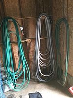 Photo showing multiple garden hoses of green and gray colors coiled and hung on wooden racks inside a shed