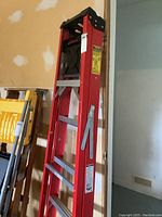 Front angled view of red fiberglass step ladder fully collapsed showing the construction and metallic steps
