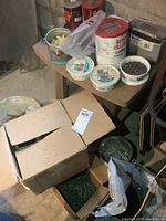 Photo showing boxes and buckets containing various nails, screws, and spirals near the small wood table.