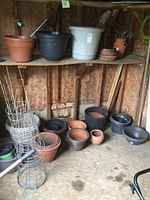 Full view of shelves and floor with multiple clay and plastic planters, some stacked, with tomato cages on the floor beside them