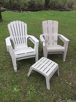 Two resin Muskoka style chairs and a matching resin footstool arranged outside on grass, showing overall set