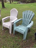 Two resin Muskoka style chairs, one beige and one faded blue-green, placed on grass outdoors with some outdoor wear visible.