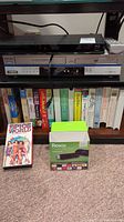 Roku Streaming Stick in box, Spice World VHS tape, and a shelf with media items including VHS tapes underneath electronics.