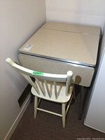 Photo showing table with both drop leaf sides down and wooden chair placed behind it.