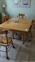 Photo showing the rectangular wooden kitchen table with four matching chairs around it, placed on tile floor. Table has caster wheels on legs and appears to have a 12-inch leaf inserted in the center.