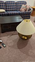 Wooden hinged coffee table and large glass base lamp next to a plaid couch and a side table