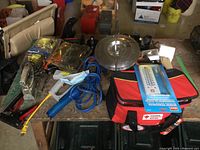 Overview of the items laid out on a wooden surface including the stainless steel pot, blue air compressor, red and black bag with thermometer on top, cords, masks, and various tools.