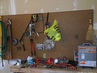 View of pegboard with multiple tools including bow saws, bolt cutters, hand tools, safety goggles, tool set box on workbench below