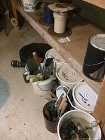 Photo showing buckets filled with drywalling and cementing hand tools with wooden handles, cement containers labeled 'Cement Type S', and wire spools on a shelf.