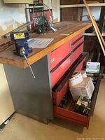 Full view of metal-framed workbench with butcher block top showing seven red drawers and vice mounted at front left
