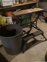 Side view of Work Mate workbench with wooden top and metal base next to large plastic garbage can
