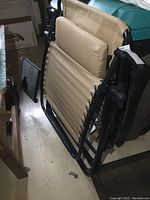 Folded tan camp chair showing black metal frame and lacing detail, with attached black side table folded alongside.