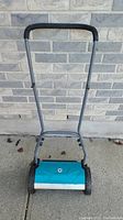 Front view of a turquoise 15 inch manual reel lawn mower with a gray metal frame and padded handle.