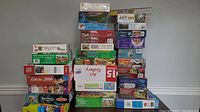 Stack of multiple puzzles of different sizes and themes including floor puzzles, animal and landscape images