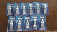 Overview of eleven new sealed Weldbond Universal Adhesive tubes in blister packaging, arranged on a wooden surface.