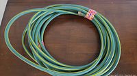 Coiled green garden hose with yellow stripes secured by colorful floral patterned tape on the wooden surface.