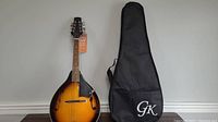 Full view of the mandolin alongside the black soft carrying case with GK logo