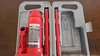 Red MotorMaster hydraulic bottle jack disassembled in molded gray plastic case, including main jack body and two red handle parts.