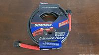 Simoniz pressure washer extension hose packaged in branded cardboard holding the coiled hose, showing hose connectors and brand logo.