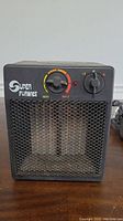 Front view of the black Super Furnace heater showing control knobs, mesh front, and power cord.