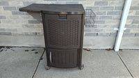 Full view of brown Suncast resin deck cooler on caster wheels with side metal basket and hinged top cooler lid.
