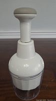 Full view of the white and clear plastic Pampered Chef veggie chopper showing the plunger top and container base.