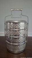 Side view of the 4-piece stacked tiffin lunch box showing intricate floral engravings on each tier and the secure latch on side.