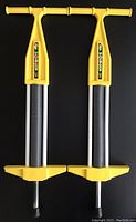 Front view of two 1980s yellow Pogo-Roo pogo sticks showing handles, spring covers and foot pedals
