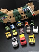 Photo showing military Chinook helicopter toy and 13 small miniature vehicles in various colors and styles.