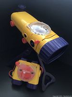 Front and side views of the yellow ViewMaster projector on tripod with red knobs and clear reel window.